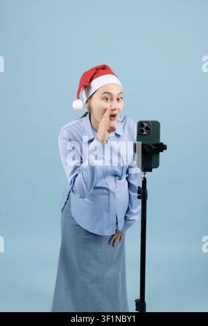 Happy young woman in santa hat singing into microphone indoors in the studio Stock Photo