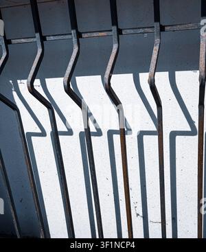 Geometric metal window bars with harsh sunlight casting sharp shadows on a white wall. Stock Photo