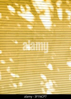 Abstract background of yellow metal shutter slats with dappled tree leaf shadows. Stock Photo