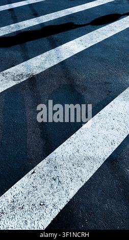 Close-up of white pedestrian crosswalk zebra lines on dark blue-toned asphalt. Stock Photo