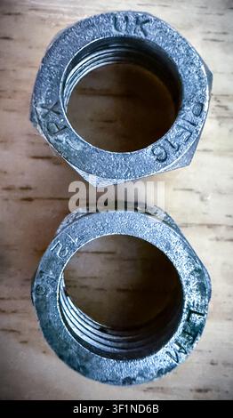Close-up of two industrial metallic threaded nuts with markings on a wooden surface. Stock Photo