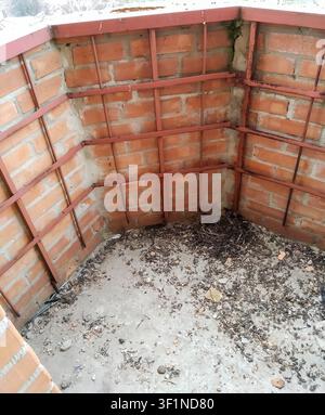 An interior view of a neglected room with brick walls, metal supports, and a floor covered in trash and debris Stock Photo