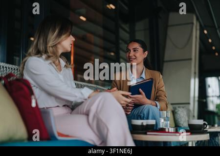 Two colleagues having a casual remote work meeting in a modern cafe lounge Stock Photo