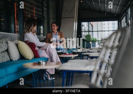 Two colleagues having a casual remote work meeting over coffee in a modern outdoor cafe Stock Photo