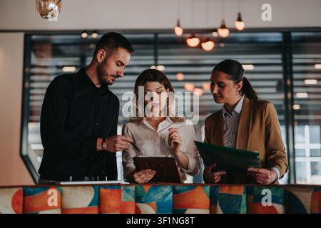 Three colleagues collaborating over a tablet during a remote work meeting in a modern office Stock Photo