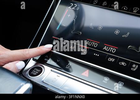 Female hand touching seat heating icon on digital climate control panel inside premium auto. Close-up viewpoint on dashboard console activating vehicl Stock Photo