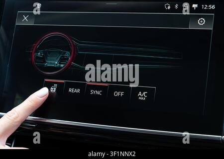 Female hand touching steering wheel heater icon on digital climate panel inside modern vehicle. Close-up viewpoint on dashboard console monitor activa Stock Photo