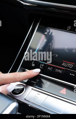 Female hand touching seat ventilation icon on digital climate control panel inside premium auto. Close-up viewpoint on dashboard console activating ve Stock Photo