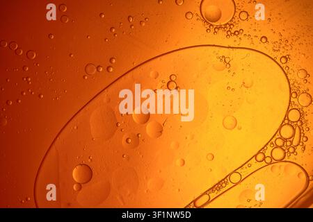 Oil drops creating an abstract bubbly pattern on an orange and yellow fluid surface Stock Photo