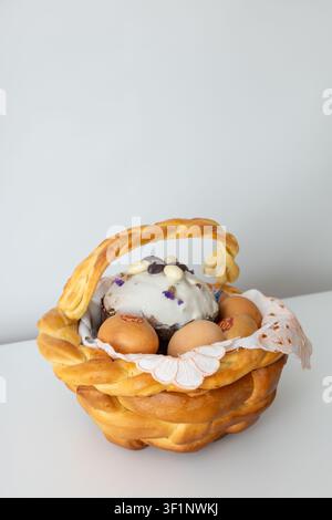 Braided golden bread basket holds white frosted cake with dried flowers chocolate eggs alongside dyed brown eggs on lace napkin. Soft lighting highlig Stock Photo