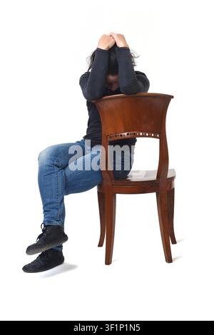 Front view of a woman sitting in a chair looking down, covering her head with her hands, with the chair turned against a white background. Stock Photo
