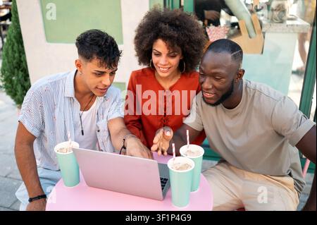 Friends bond through digital experiences, exploring content together on a laptop enjoying technology Stock Photo
