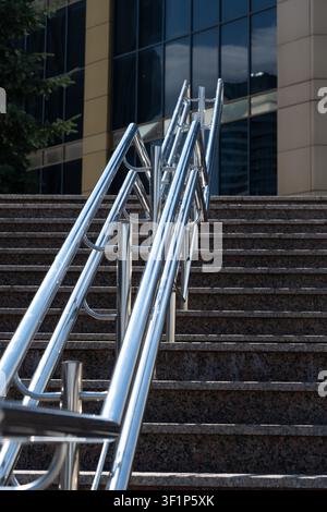 A Close-Up View of Modern Stainless Steel Handrails Along Stairs Leading Up to a Tall Glass Building Under Clear Blue Skies Stock Photo
