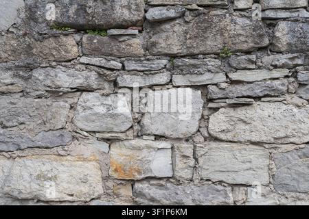 Weathered stone wall built from irregular natural rocks and mortar. Rustic masonry texture for architecture, restoration and design. Stock Photo