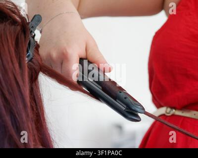 Hair stylist using a flat iron to straighten long red hair during wedding preparation Stock Photo