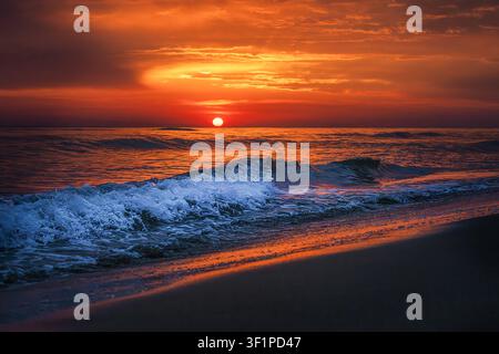 Dramatic Red Sunset Over Ocean Waves on Beach Stock Photo