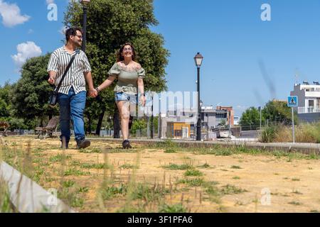 Happy couple walking holding hands in park on sunny day Stock Photo