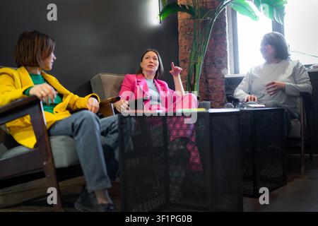 Group of women at table by window in sunny cafe, smiling and talking in business casual style. Cafe, women, window, daylight, business casual. Stock Photo