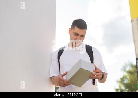 A smiling guy holds a parcel outside on a sunny day Stock Photo