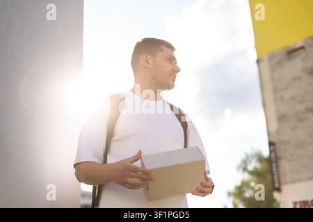 A smiling guy holds a parcel outside on a sunny day Stock Photo