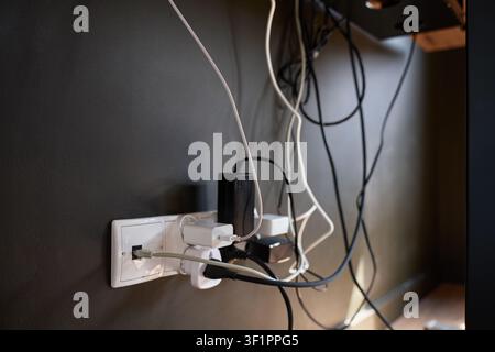 Close up of wall outlet with connected adapters, plugs and tangled cables. Concept of home electronics and multiple device charging Stock Photo