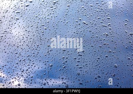 Raindrops on Glass Against a Blue Cloudy Sky. Clear raindrops cover a glass surface against a softly blurred blue and cloudy sky. Stock Photo