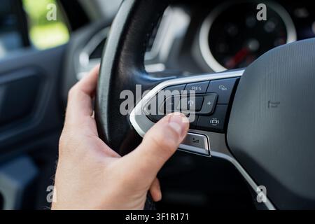 Man adjusting cruise control settings on a smart steering wheel with multi-function buttons during a vehicle commute showing interior details Stock Photo