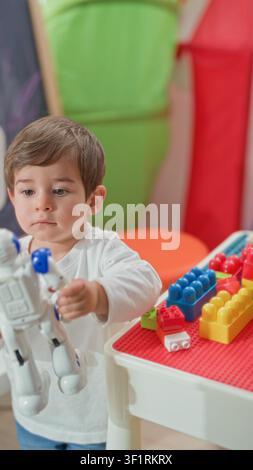 Boy holding white toy robot over a table with colorful building blocks in a playroom tent; curiosity imaginative play. Stock Photo