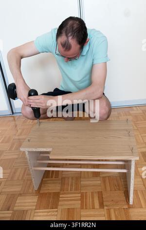 Father using cordless drill while assembling a wooden storage bench in home DIY project Stock Photo