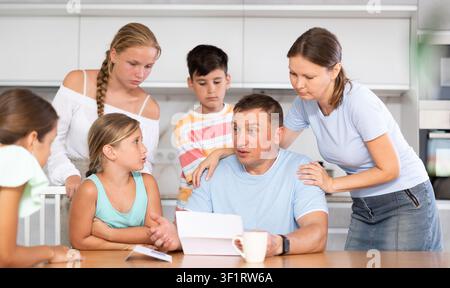 Frustrated man sits in kitchen next to family and reads unpleasant news in letter. Stock Photo