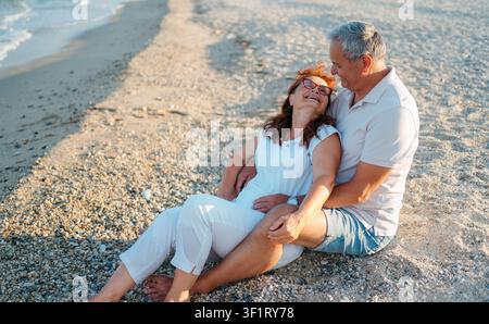 Senior couple sitting hugging on the beach Stock Photo