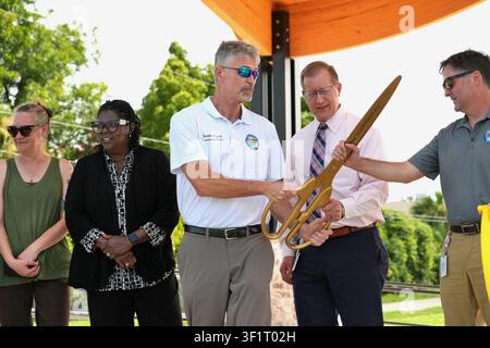 Panama City, FL, USA. 14th Jul 2026. Ward 1 Commissioner Robbie Hughes passes the City of Panama City's giant gold ceremonial scissors to fellow officials moments after the ribbon cutting that officially reopened Millville Waterfront Park on Watson Bayou. The Community Redevelopment Agency-funded overhaul - amphitheater, lighted walking path, playground and picnic shelters - finished about $200,000 under budget, part of a citywide parks reinvestment push in the historic working-class mill neighborhood hard-hit by Hurricane Michael in 2018. Credit: Tosh Persons / Ģ����ý Live News Stock Photo
