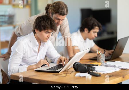 Friendly adult man helping young male colleague in work in coworking space Stock Photo