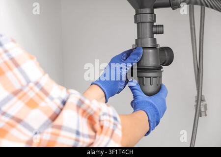 Plumber in blue gloves installing a new sink trap under a kitchen or bathroom basin, home renovation and repair concept, the hands are carefully conne Stock Photo