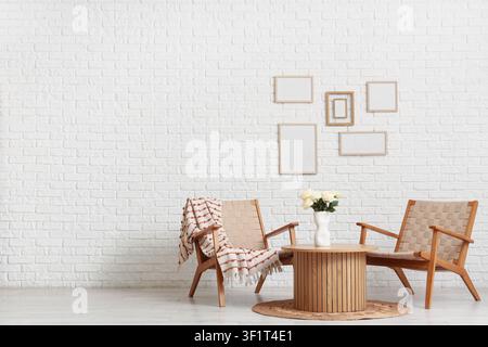 Modern living room interior with two wooden armchairs round coffee table white roses and blank picture frames on a white brick wall Stock Photo