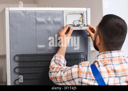 Repairman fixing a refrigerator with exposed wiring and condenser coils, appliance maintenance and home service Stock Photo