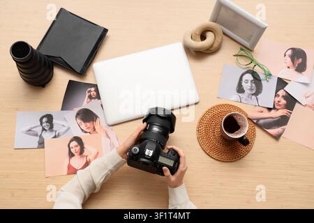 Photographer holding a professional dslr camera with a laptop and printed model photos on a wooden desk, top view Stock Photo