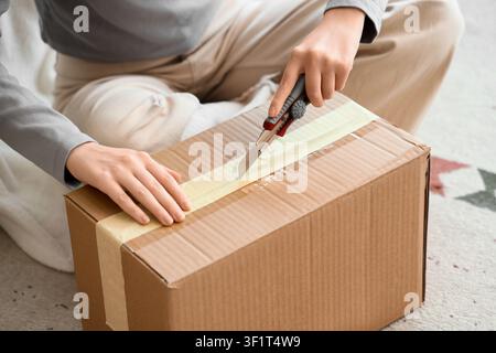 Person opening a cardboard box with a utility knife, online shopping delivery and unboxing experience, the hands carefully cut through the tape on the Stock Photo