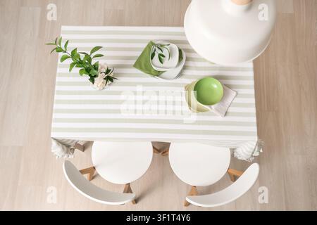 Dining table with striped tablecloth, modern chairs, and minimalist place settings, overhead view Stock Photo
