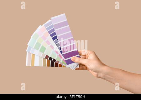 Hand holding a fanned color swatch book with various shades of purple, green, pink, and brown on a beige background Stock Photo