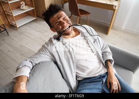 Electrocuted young man with burnt face and plug in his mouth at home Stock Photo