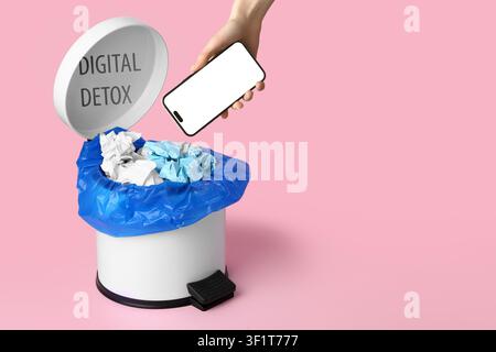 Hand putting a smartphone with a blank screen into a trash can labeled "digital detox" on a pink background, the trash can lid displays the words "dig Stock Photo
