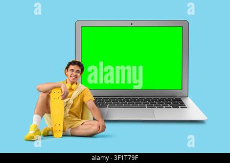 Smiling young man with skateboard and headphones sitting next to a laptop with a green screen Stock Photo