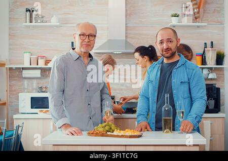 Extended family gathers in a modern kitchen for a video call, using online webcam communication during a relaxed home moment, around a shared kitchen table in a home dining setting. Stock Photo