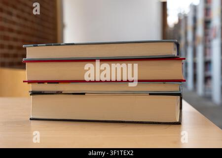 A close-up horizontal shot of a stack of three thick hardcover books lying on a light wooden table. The middle book features a distinct red edge or bo Stock Photo