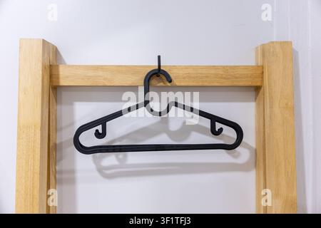 A black plastic clothes hanger hanging on wooden frame casting soft shadow in minimalist interior, simple household object conveying neat organization Stock Photo