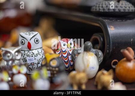 A colorful ceramic owl figurine among assorted small souvenir animals and trinkets on market table, vibrant handcrafted detail and shallow depth of fi Stock Photo
