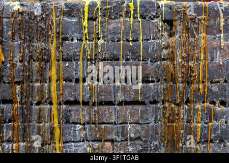 A melted colored wax dripping down rough brick wall, yellow and brown streams creating textured vertical patterns and weathered, layered surface with Stock Photo