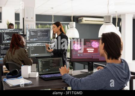 Male programmer troubleshoots crashed software program in busy startup office, representing modern teamwork and collaboration while resolving coding failure during online security incident. Stock Photo