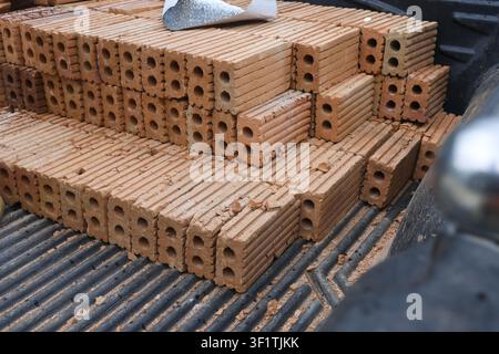 A stack of rectangular clay hollow bricks with ribbed faces and circular cores, dusty construction cargo on truck bed conveying raw building material Stock Photo
